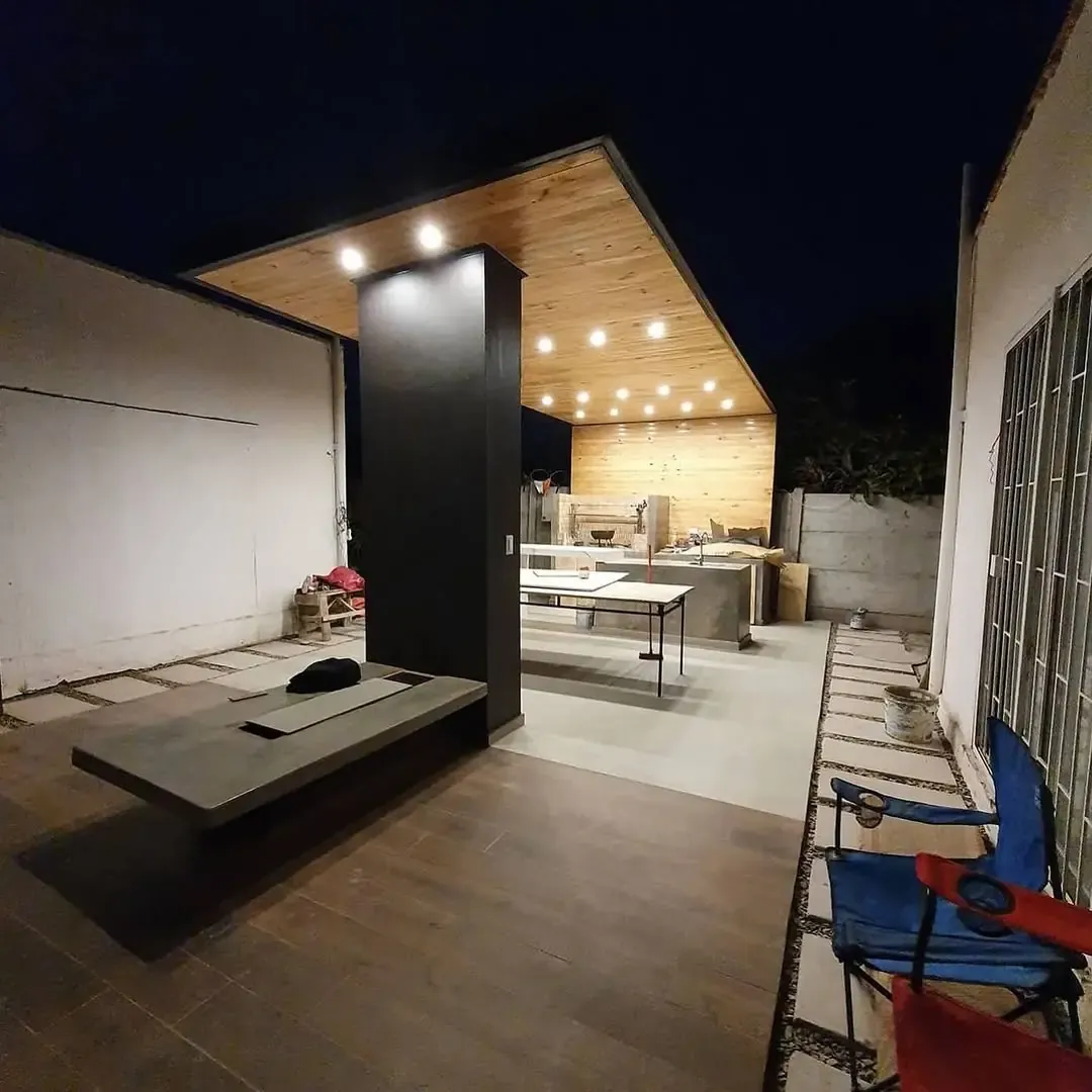 Terraza cubierta de diseño moderno, con estructura de metal, cielo de madera e iluminación lineal empotrada, de noche
