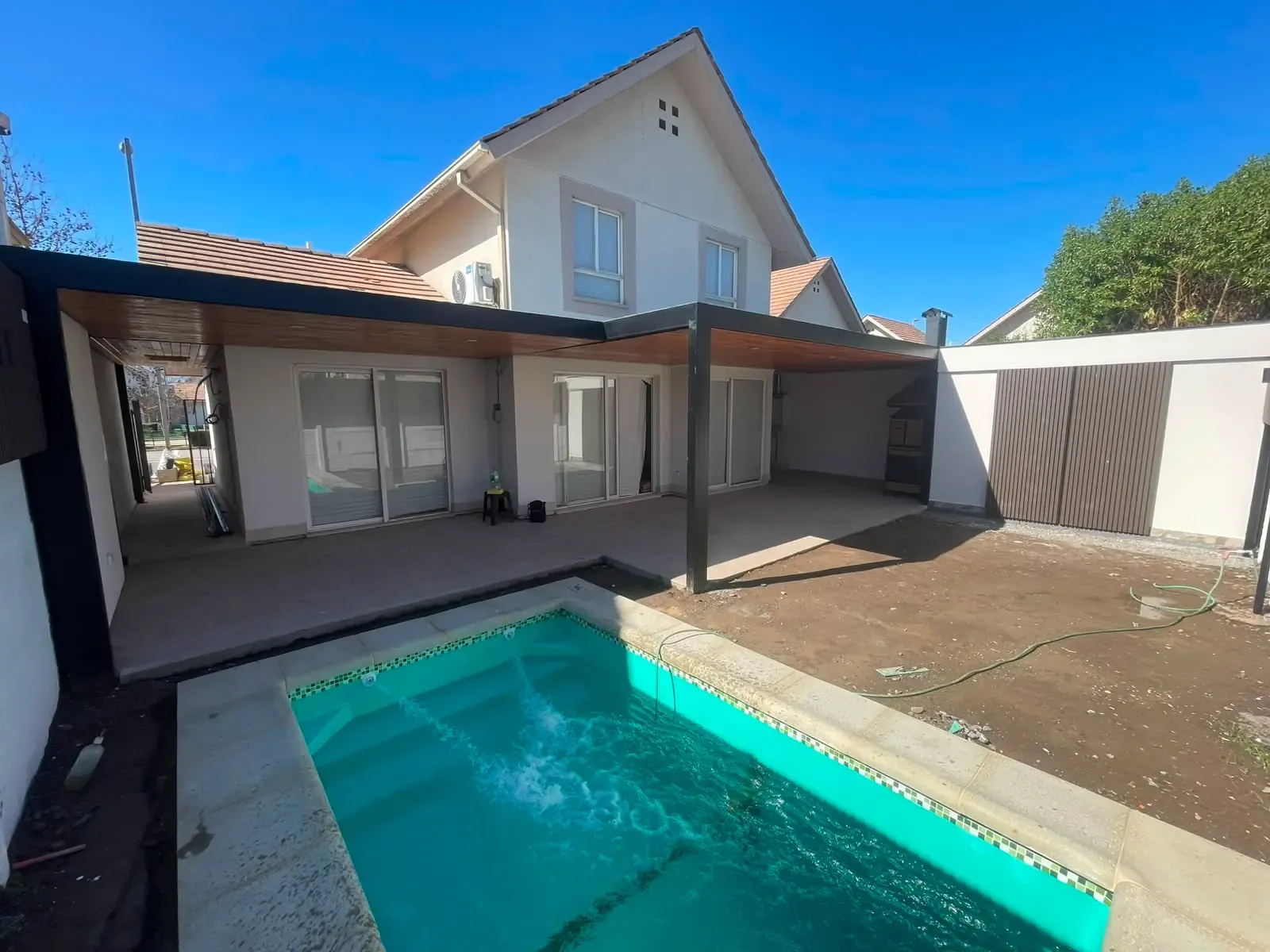 Terraza cubierta con estructura de metal y cielo de madera, junto a una piscina con bombas de filtrado en funcionamiento